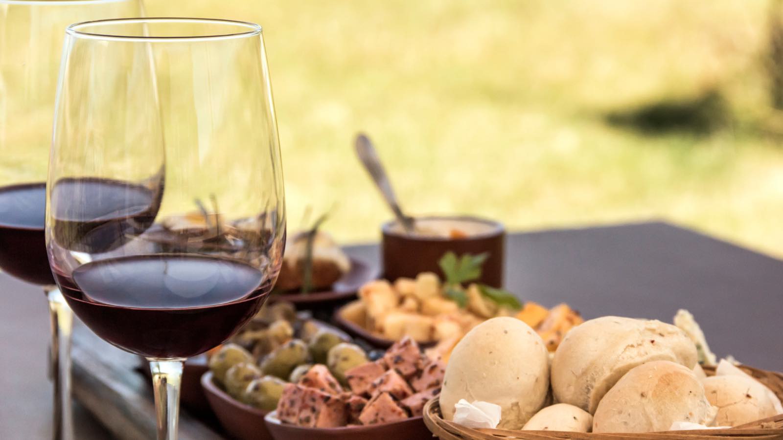 A charcuterie board of cured meats, olives and breads beside glasses of red wine