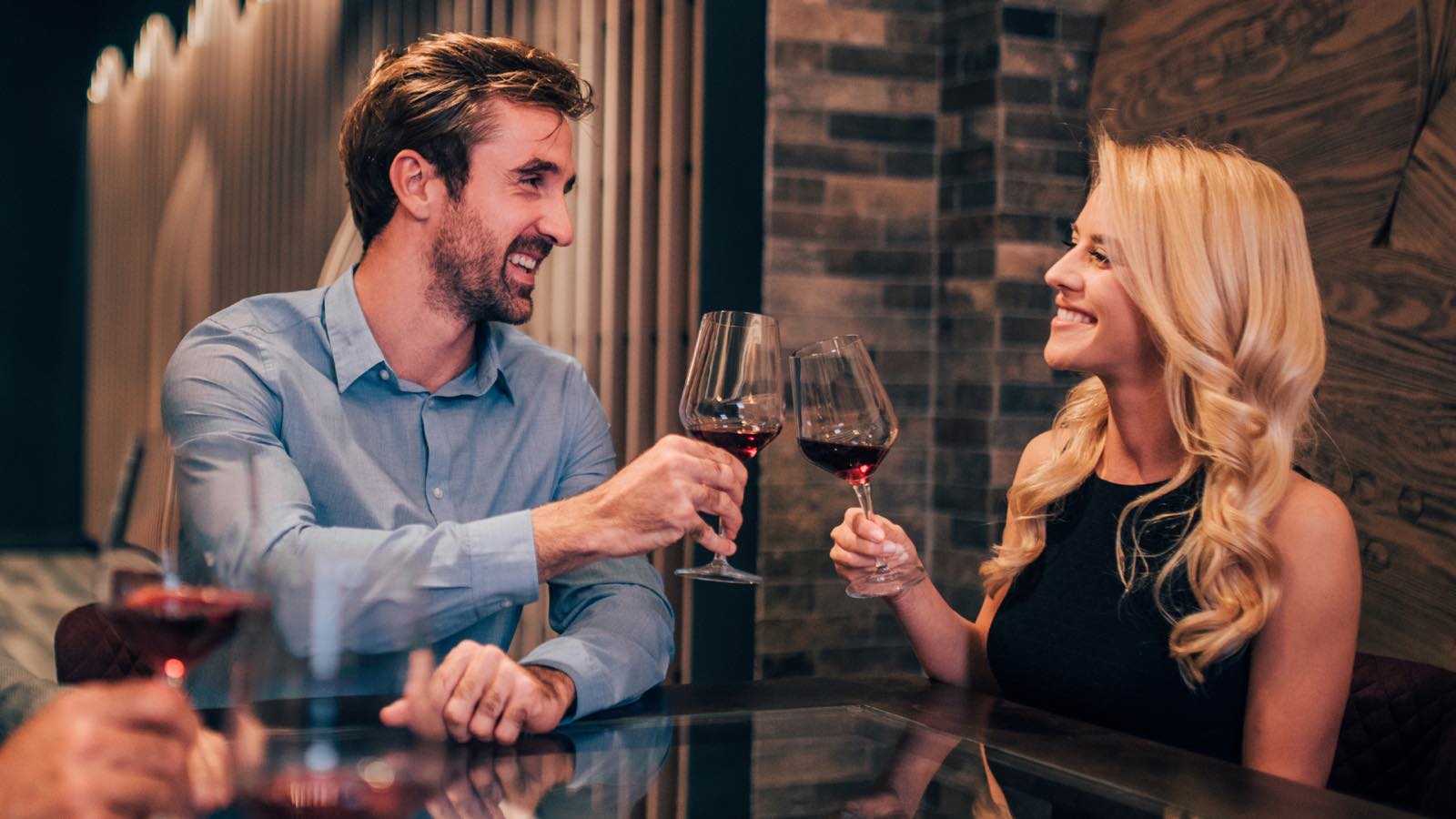A couple raising glasses of red wine together across a table