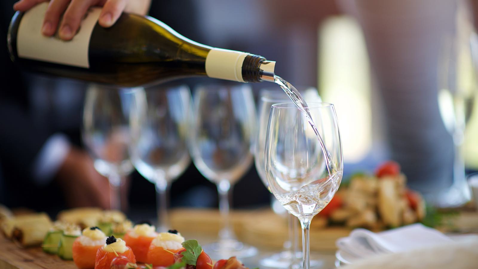 White wine being poured into a glass beside a spread of small plates