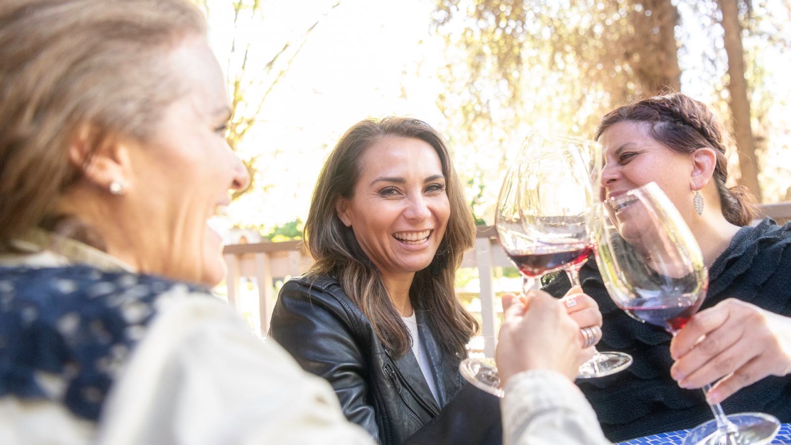Three friends laughing together over glasses of red wine outdoors